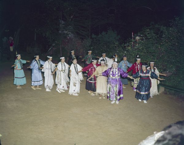 Slightly elevated view of a group of Winnebago (Ho-Chunk) Indian women, dressed in ceremonial clothing, dancing the Swan Dance.
