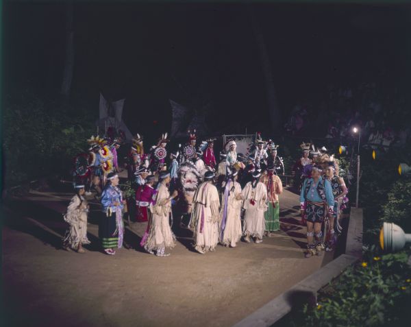 A group of Native American Indians, dressed in ceremonial clothing, perform the Snake Dance at the Stand Rock Indian Ceremonial Snake Dance. The women are in a line in the center, while men line up on either side.