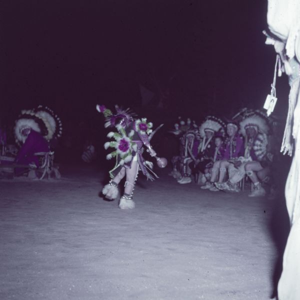 A dancer is performing the Eagle Dance as a crowd is watching from the side.