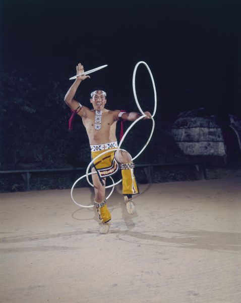 Spencer Jane, hoop dancer, free-twirling 5 hoops. One hoop is in his right hand, and the other four are interconnected through his legs, hips, and left hand. 