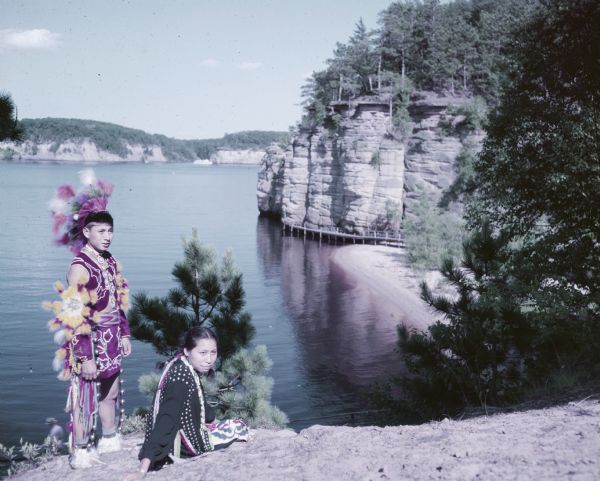 An unidentified young man is standing next to an unidentified young women sitting on a rock over looking Palisades and Big Bay. 