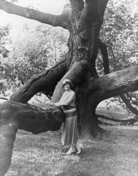 Charlotte "Lottie" (Mrs. Walter) Kohler posing standing with her forearms resting on the branch of a large, spreading tree on the grounds of the Kohler estate "Riverbend." Her husband, Walter Kohler Sr., was owner of the Kohler Company and one-term governor of Wisconsin, 1929-1931.