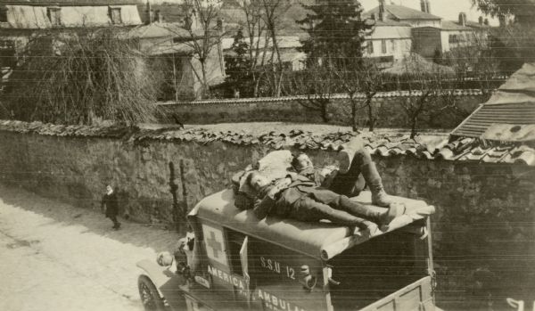 Elevated view of two men sleeping on top of an ambulance during the day. Captioned: "Faith and Benny, both in aviation now, asleep on top of the latter's ambulance on the first day of spring, Ste. Menehould."