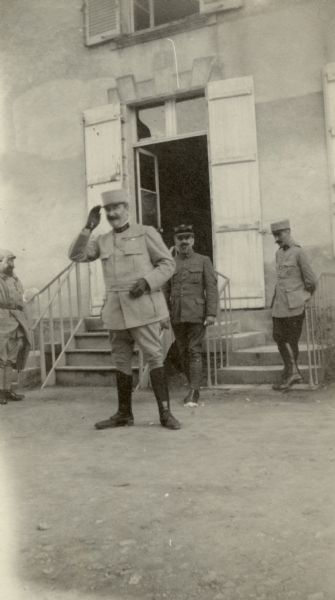 Three men and a colonel standing outside the entrance to a building after being decorated. Captioned: "Colonel Couillaud, saluting stretcher-bearers, the men he has just decorated. Notice his string of service ribbons."