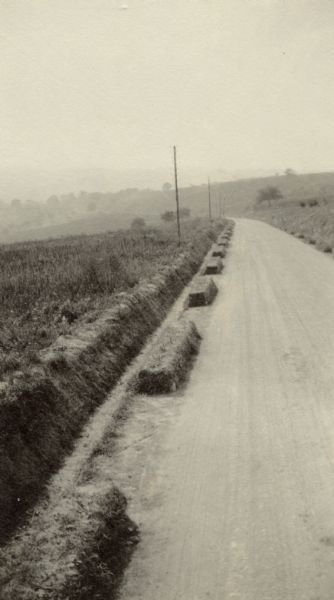 Elevated view of a well-paved road in a war zone, surrounded by piles and fields of hay. Captioned: "A typical road in the War Zone. Wild, smooth, well graded and permanent, it is."