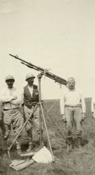 Three men standing behind a machine gun. Captioned: "A Hotchkiss machine gun, operated by a 48-year old crew of Frenchman. These men were mobilized."