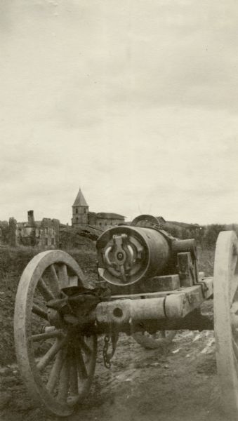 The breech of a cannon is in the foreground on a muddy road, and buildings are on a low hill in the background. Captioned: "The breech of a field gun lying innocently by the road-side near Verdun."