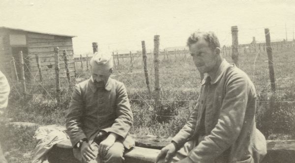 Two prisoners sitting outdoors at their prison camp. Captioned: "Boche prisoners at Saint Hilaire."