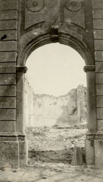 View through arch of a church left in ruins. Captioned: "The church at St. Thomas, with one wall, the roof and altar shot away. Notice the position of the Virgin at the right."