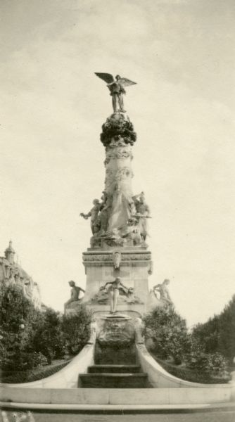 A statue with bushes planted at the base. Captioned: "Reims. The artistic statue of Victory. Notice the delicacy of the work."