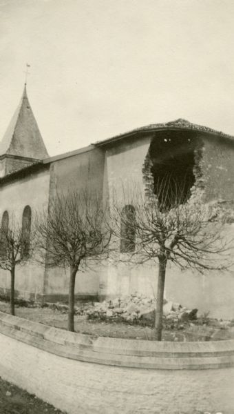 A church with a hole in the wall. Captioned: "The hole made by a Boche shell entering the Dombasle church. It exploded inside and left little except ruins."