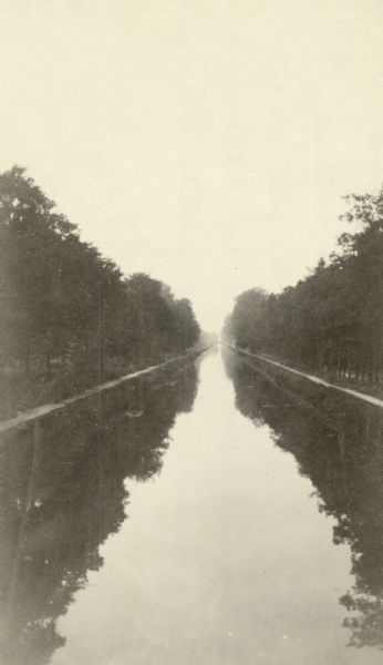 A delivery road in France, filled with water reflecting the trees on both sides. Captioned: "A typical tree-lined country road in France. In delivery at night over such roads, it is necessary to guide by the path between the trees overhead."