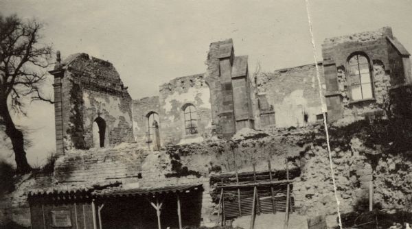 Exterior view of a damaged church that is missing walls and a roof. Captioned: "Church showing 'the wall which isn't there.' St. Thomas."