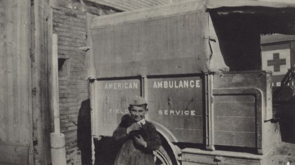 A young boy, standing in front of an ambulance, posing for a portrait with mascot puppy in his arms. Captioned: "'The Petit goss' with our pup mascot. He was stolen later."