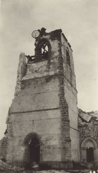 Exterior view of a damaged church tower, with a clock at the top. Caption reads: "Ruined church at St. Hilaire-le-Grand. Notice the clock."