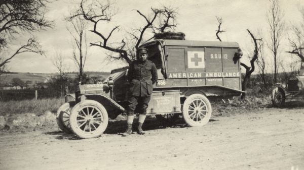 View across road towards a man standing in front of an ambulance. Caption reads: "Two months out of Paris. Taken the day he left Wambasle en route for Waly, Seward, and Ste. Menehould."