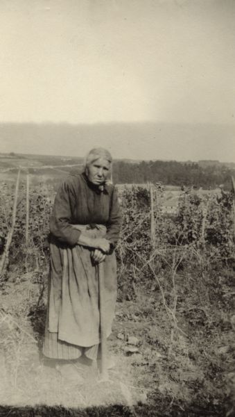 Outdoor portrait of a woman standing in front of her vineyard. Caption reads: "A chic French Heart-breaker, snapped posing in her vineyard. Near Vaux Varennes."