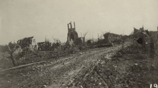 View down road leading to what is left of Esmes. Caption reads: "What is left of Esmes. Notice the shell-packed road and the concrete water trough."
