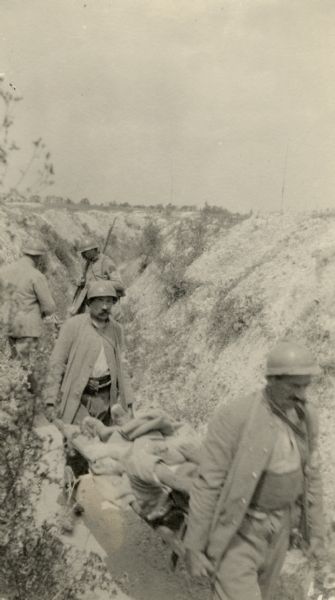 Two soldiers carrying an injured man through the trenches. Caption reads: "Brancardiers [stretcher-bearers] carrying in a wounded pirla."