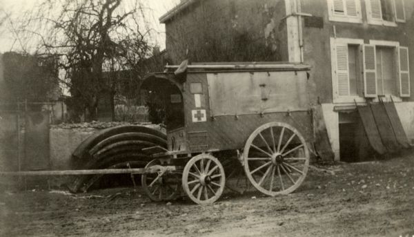 A horse ambulance parked on a road near buildings. Caption reads: "A horse ambulance frequently used to carry wounded from batteries to "poste de secours" but more frequently to carry the dead."
