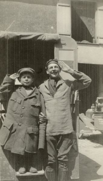 Portrait of a man and child posing in front of an ambulance. Caption reads: "Robineau Cook, as a French marine, and a 'petit goss' as an ambulance driver. St Menehould."