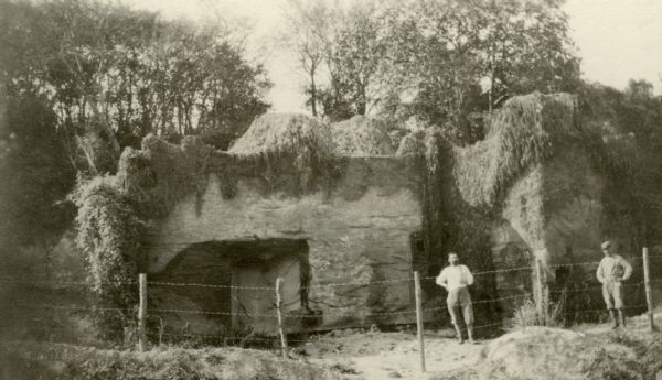 Two men standing near camouflaged telephone headquarters. Caption reads: "Not a rocky cliff at all but a neatly camouflaged telephone headquarters on the road to Bouleuse in the Aisne country."