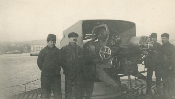 Four men posing with a large gun on the deck of a ship. Caption reads: "140 m/m gun on stern of French liner 'Rochambeau' on which I returned to America. ('U-boats' carry no larger pieces that[sic] 105 m/m (4 inches)."