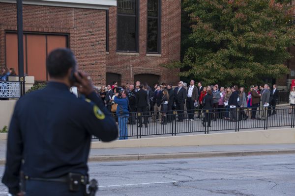 An African-American police officer in the foreground  is talking on a phone or walkie-talkie while he is surveying the line of men and women waiting to enter the Republican presidential debate.