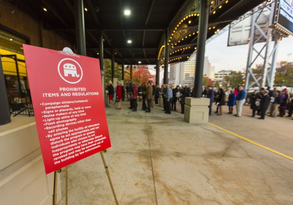 A red sign, bearing an image of the Republican elephant, on an easel. It lists items not allowed within the Republican presidential debate and the basic rules of decorum. In the background is a line of people waiting to enter the Milwaukee Theater which is hosting the debate.