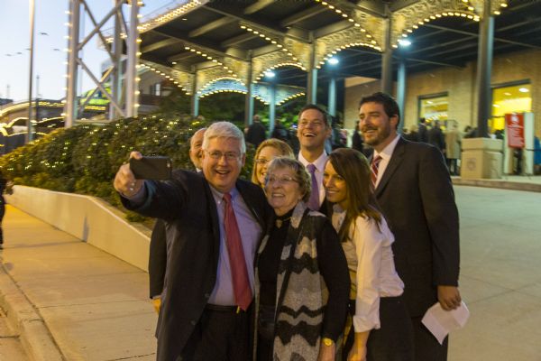 Group portrait of a family standing in a tight group to take a "selfie" while standing outside the Republican presidential debate at the Milwaukee Theater. A man in a suit is standing next to a woman as he is holding up his smart phone for the picture. The younger members of the family (two women and three men) stand behind the couple, all smiling.