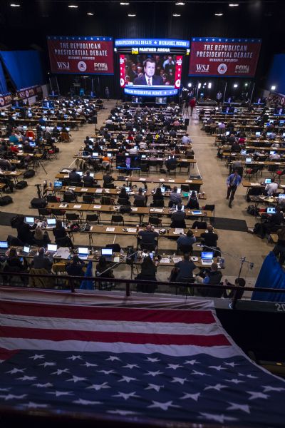 View down bleachers, covered with an American Flag, towards the media on the floor of the Panther Arena at the Republican presidential debates. One of the moderators, Neil Cavuto, is on the large screen at the back of the room broadcasting the debate.