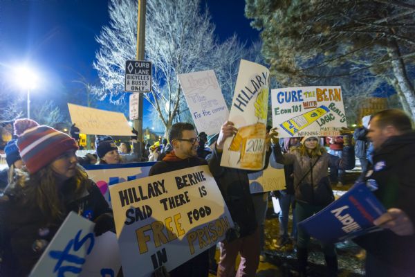 A supporter of Hillary Clinton confronting a group of anti-Hillary demonstrators. Both groups are holding up signs.