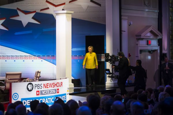 View over the audience towards the U.S. Secretary of State, Hillary Clinton, walking onto the stage for the Democratic presidential debate. A camera operator is following her.