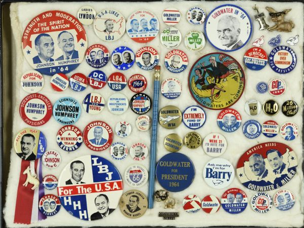 Framed assortment of political campaign buttons for Lyndon B. Johnson and running mate Hubert Humphrey, and Barry Goldwater and running mate William E. Miller. Most of the buttons are the standard round buttons with the names, slogans, or portraits of the candidates. Two are in the shape of a donkey and an elephant, both wearing Goldwater's iconic eyeglasses. Another is a lenticular, or flasher, button, which shifts from an image of Johnson next to a donkey telling his wife: "Start Packing," to an image of Goldwater and his wife riding an elephant and stating: "Goldwaters are Coming."
