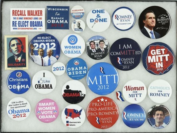 Framed assortment of political campaign buttons for Barack Obama and running mate Joe Biden, and Mitt Romney and running mate Paul Ryan. Two of the buttons supporting Obama also support the recall of Wisconsin Governor Scott Walker. One reads: "Recall Walker, Re-Elect Obama, This Is What Democracy Looks Like." The other button primarily consists of the red and blue portrait of Obama, but instead of the more typical 'Hope' or 'Change' reads "Solidarity" and features a small image of the Wisconsin fist. Both are from citizensprotest.org.