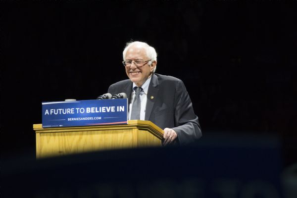 Bernie Sanders, U.S. Senator from Vermont, smiling while standing behind a podium during a rally held in the Kohl Center. A sign on the podium bears his campaign slogan: "A Future to Believe In." 