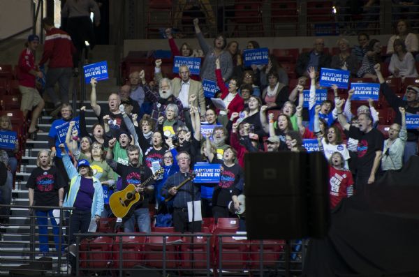 The Solidarity Sing Along group singing at the Bernie Sanders rally being held in the Kohl Center. They are holding signs and have their fists in the air. Two men are playing a guitar and a mandolin. 