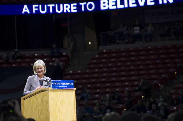 Former Wisconsin Lieutenant Governor Barbara Lawton standing behind the podium and addressing the audience at the Bernie Sanders rally held in the Kohl Center. A lighted sign high up in the background is spelling out Sanders' campaign slogan: "A Future to Believe In."