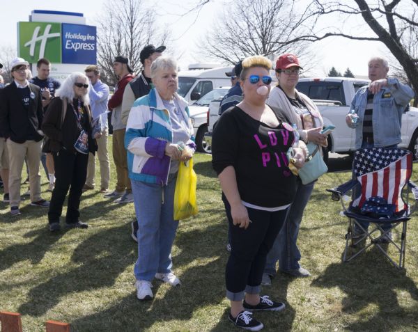 A line of men and women waiting outdoors to enter the Donald Trump rally held in the Janesville Conference Center. Many of the people are wearing shirts, pins, or lanyards in support of Trump.