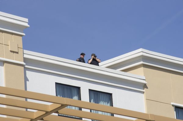 View looking up at two police officers standing on the roof of the Janesville Conference Center at the Holiday Inn Express which is hosting the Donald Trump rally. One of the male officers is looking through a telephoto zoom lens. 