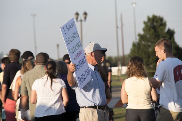 A man is standing near a line of people waiting to enter the Donald Trump rally and holding a sign which reads: "I support religious tolerance and America's immigrant tradition." A police officer is standing in the background.