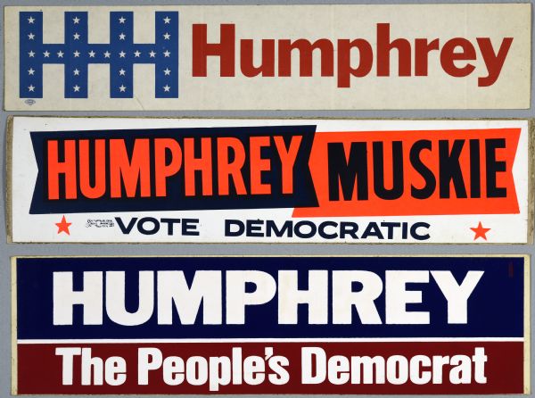 Bumper stickers for Hubert Horatio Humphrey and Edmund Muskie. The top bumper sticker has blue and red text on a white background that reads: "HHH Humphrey." The middle bumper sticker has orange stars, and orange and blue type on a white, blue and orange background that reads: "Humphrey, Muskie, Vote Democratic. The bottom bumper sticker has white type on a blue and red background that reads: "Humphrey, the People's Democrat."