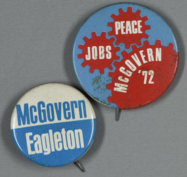 Two presidential political campaign buttons for George McGovern and Thomas Eagleton. The lower left button is blue and white and reads: "McGovern / Eagleton." The top right button is blue with red gears and white text, which reads: "Jobs," "Peace," and "McGovern '72."