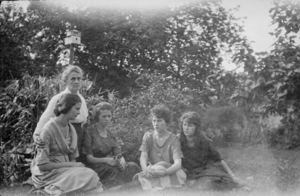 Cora Judkins, kneeling, posing with her four daughters sitting in front of her. They are, from left, Bonnie, Leonore Judkins Middleton, Juanita and Blanche. There is a small patch of corn behind them on the left, and a birdhouse on a post in the background.