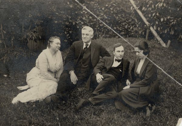 Two well-dressed couples, Mr. and Mrs. Fred E. Hagin, left, and Mr. and Mrs. Forest Middleton, reclining on a lawn with shrubbery behind them.  