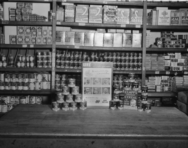 Oscar Mazursky Store, 301 West Mifflin Street, featuring a Clapps Baby Foods display with a <i>Life</i> magazine poster on the counter. Shelves are stacked with popular brands of canned goods, Arm and Hammer, Heinz, Carnation and others.