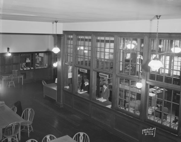 Elevated view of interior of the Madison Public Library, 206 North Carroll Street. Margaret Nordholm, on the left, and Emma Bryan on the right are standing behind the Registration and Return windows.