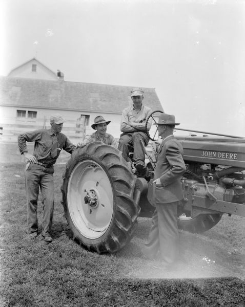 William F. Renk, wearing a suit, and his sons. Left to right are: Walter Renk, Wilbur Renk, both standing, and Robert Renk sitting on a John Deere tractor with Firestone tires. They are in the farmyard at 1000 Wilburn Road.