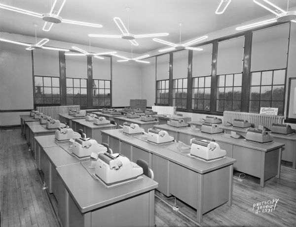 Madison Vocational and Adult Education School, 211-213 North Carroll Street. Angled view of a typing room #442 from the front of the classroom. There are lighted ceiling fans above the desks. For Haskell Desk Co.
