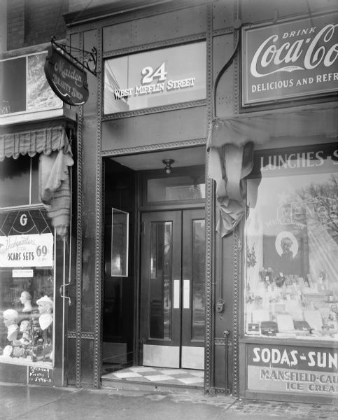 Entrance to Hub Building, 24 West Mifflin Street, showing Maiden Beauty Shop sign and part of Menges Pharmacy with a Coca-Cola sign.